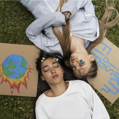 Zwei Schülerinnen liegen im Gras, neben Ihnen liegen handgemalte Plakate.